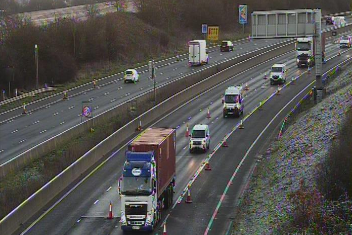 A traffic camera view of the M25 early on Friday. It is fairly clear of traffic. On the right side, cones mark out one lane (the slow lane next to the hard shoulder) which is the only lane in use. There is a 50 MPH sign on the central reservation. Mostly lorries and vans drive down the open lane.