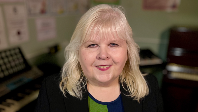 Head and shoulders image of Maria Grimmer, wearing a dark suit jacket and blue and green top