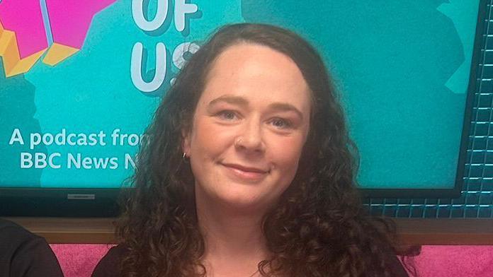 Louise McCullough. She has long dark curly hair, sitting on a pink sofa with the State of Us branding on a screen behind her.
