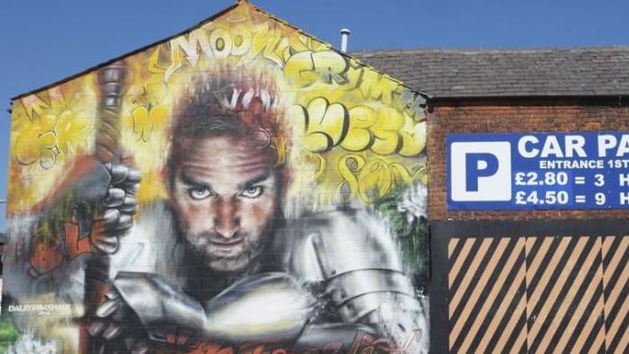 Street art on the side of a building on Topping Street, Blackpool, showing a man dressed in silver armour holding the handle of an ornate weapon