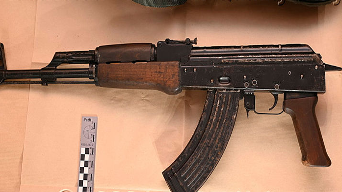 An AK-47 gun, pictured against a beige background.