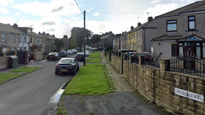 View of Dovesdale Road in Bradford, with terraced houses and cars on either side.