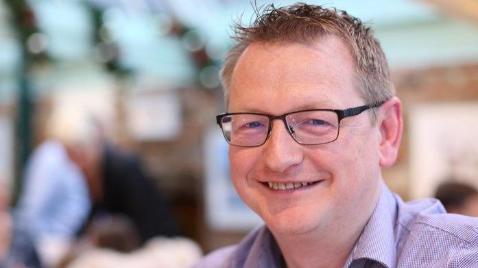 Nick Rowntree smiling at the camera, he is wearing a lilac shirt and glasses