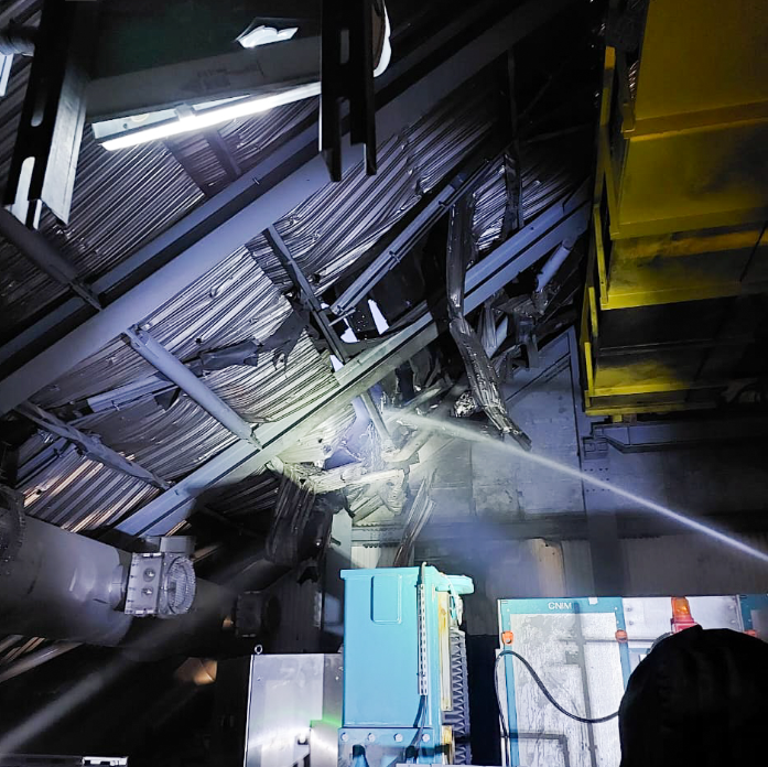 A stream of water from a hose shoots through a hole in a metal sheet roof to combat the smoulders