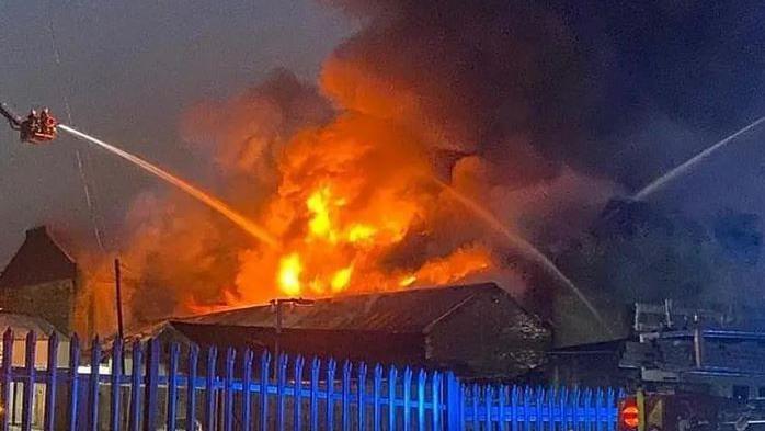 A large fire at a warehouse building, with several aerial platforms being used by the fire service. Jets of water are being sprayed on the flames from three directions, with the fire burning brightly. 