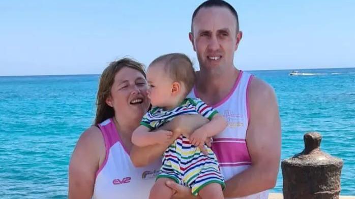 A man and a woman hold a baby standing against the backdrop of the sea