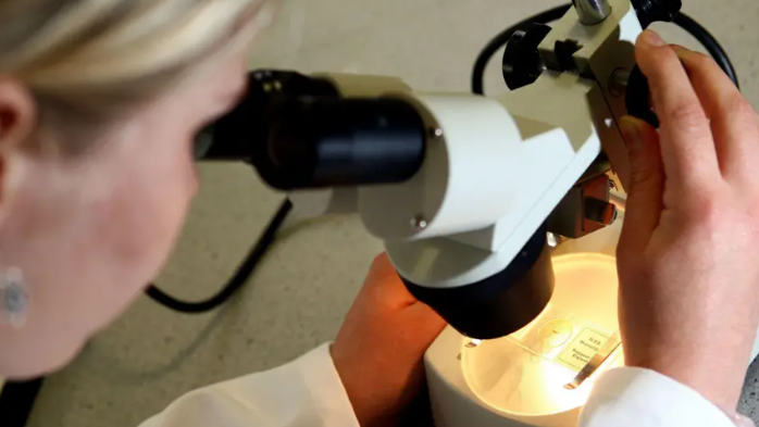 A close-up of a scientist looking through a magnifying glass.