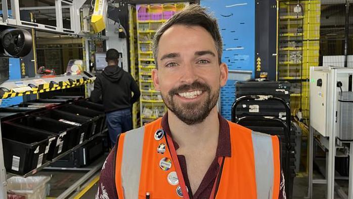 Amazon LCY3 depot General Manager John McEwen standing in front of an associate packing good for despatch