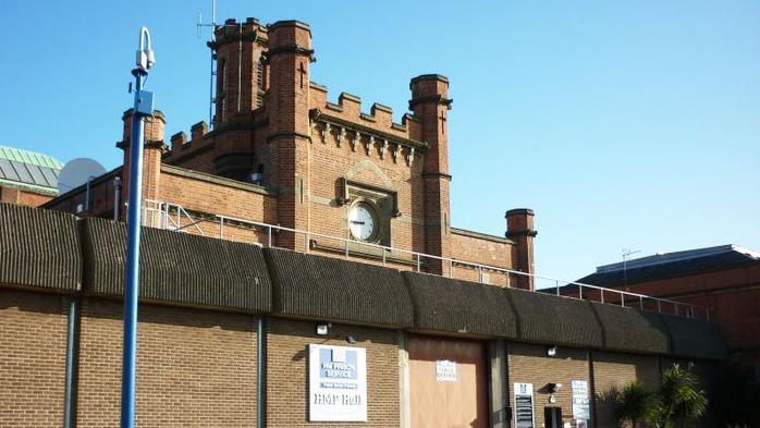 The main gate of Hull Prison it has a large wall topped with concrete barriers and a central tower with turrets and a clock