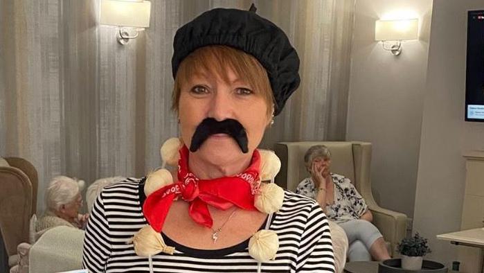 A woman in a striped top, black beret and fake moustache