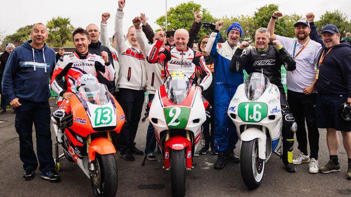 Ian Lougher sitting on his WHite and red machine, flanked by Lee Johnston on an orange bike and Stuart Hall on a white and blue bike. The three men are holding clenched fists up in celebration.