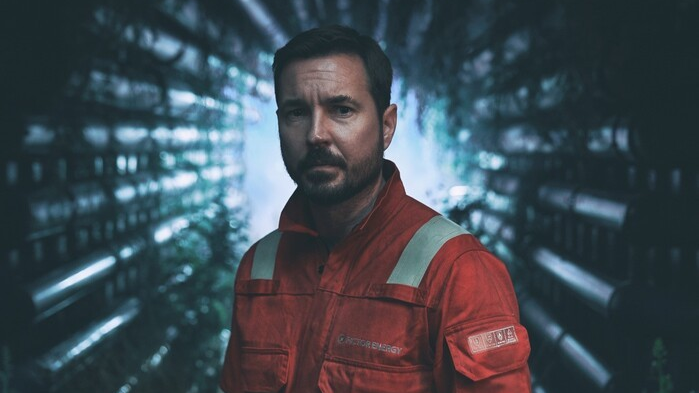 Martin Compston in character on TV show The Rig - he is looking straight into the camera, while wearing a red/orange rig worker's uniform