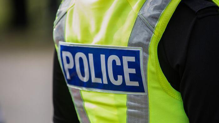 A police officer pictured from behind, showing just their torso. They are in a high-vis police vest