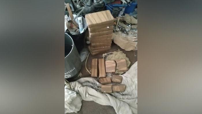 A stack of blocks of cocaine, each wrapped in brown paper, next to a grey gas cannister which has been cut open.