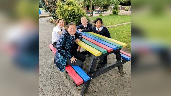 Four children smile at the camera while sitting around a rainbow coloured picnic bench