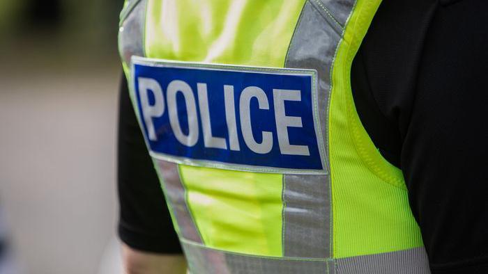 A police officer wearing a fluorescent vest, photographed from behind. It is just their torso.