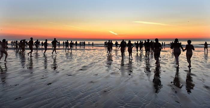 A large number of people enter the water at dawn. The bodies appear in silhouette.