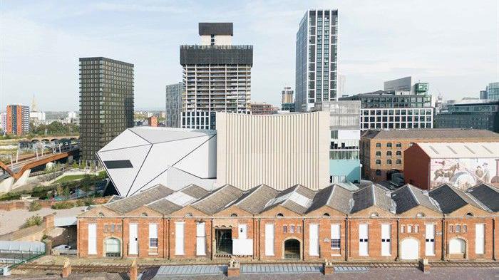 The white geometric Aviva Studis can be seen between warehouses, at the front of the picture, and the Manchester skyline at the back.