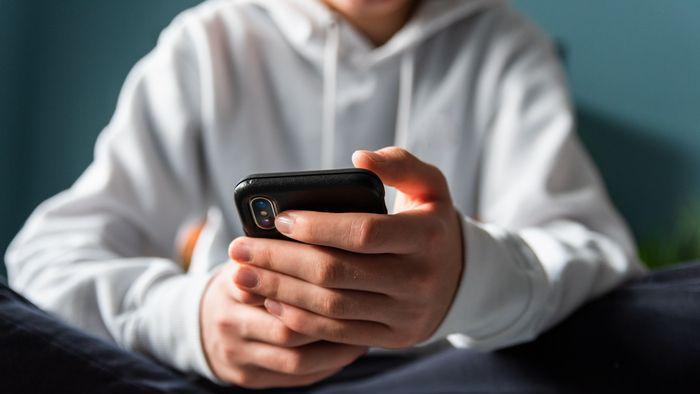 Close-up of a boy wearing a white sweater on his phone.