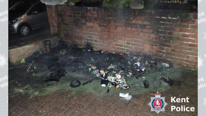 Burnt big green wheelie bins. They are disfigured, charred and half melted.