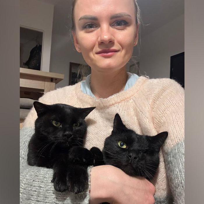 A woman with blonde hair holds two black cats