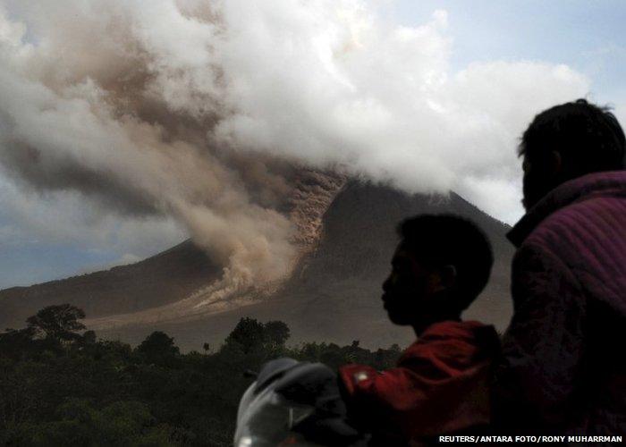 Residents sit on their motorcycle as they watch an eruption at Mount Sinabung, in Namanteran village in Karo Regency, Indonesia's North Sumatra province, June 14, 2015