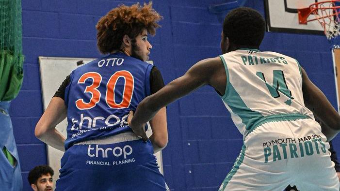 An Oxford Hoops player, wearing a blue jersey, has possession of the ball and has his back turned to an opposition player, dressed in white.