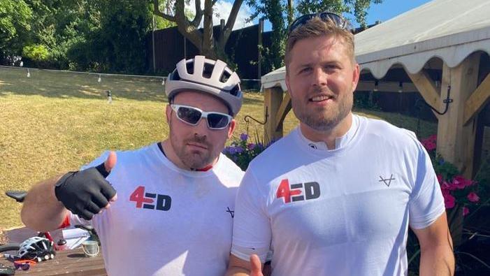 Fraser Balmain and Ed Slater in white shirts with the 4Ed logo on their chest. One is wearing a cycling helmet and the other has blonde hair with sunglasses on his head.