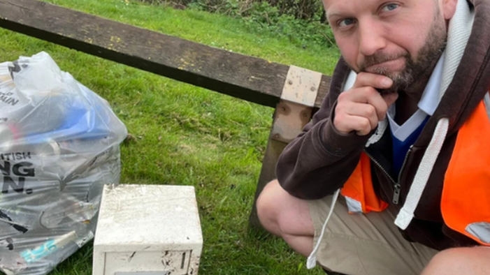 A man in high-vis kneeling by a safe and a bin bag