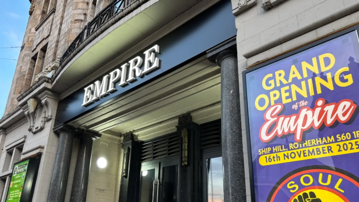 A grand entrance to a building with black marble pillars and a large purple poster with yellow writing