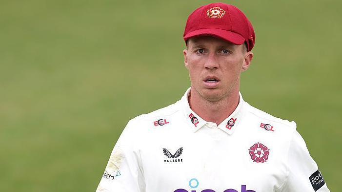 Nathan McSweeney in a white Northamptonshire shirt and claret baseball cap during a match