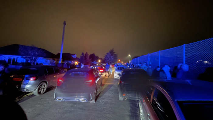 Rows of cars held up in standstill traffic. It is night time, and pedestrians are walking away from the fireworks event