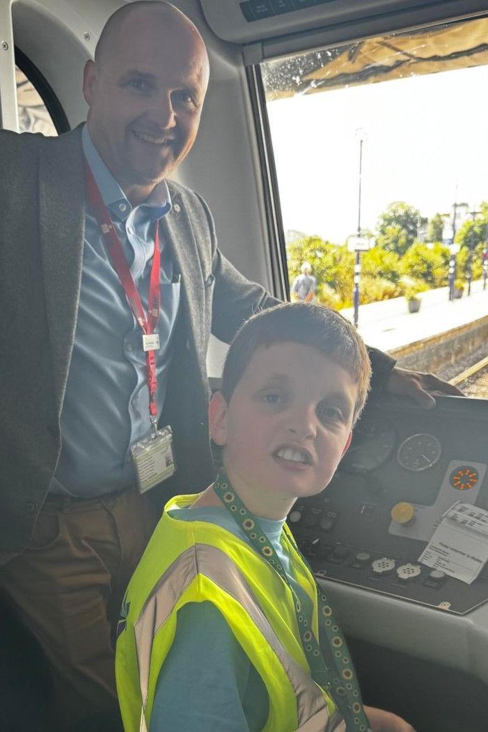 Nathaniel, wearing a hi-vis jacket, in the cab of a train with Steve Whitehead.