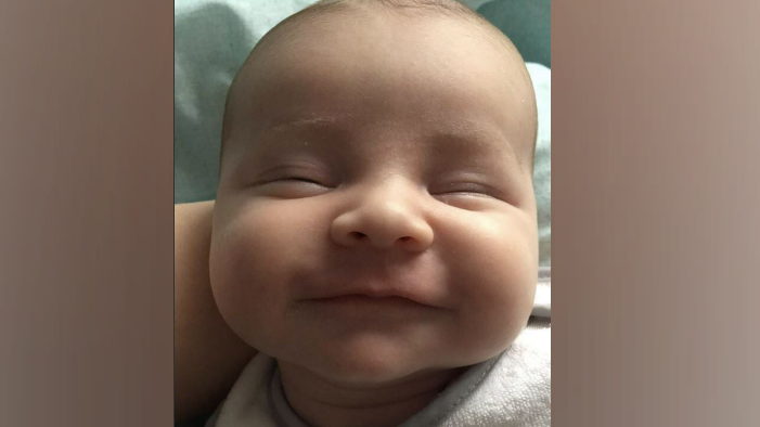 A close up image of a newborn baby smiling with their eyes closed 