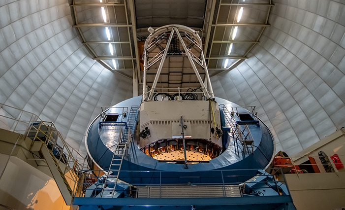 A blue telescope inside a dome. It consists of a square base on which sits a circular ring from which a thick cream coloured antennae protrudes.