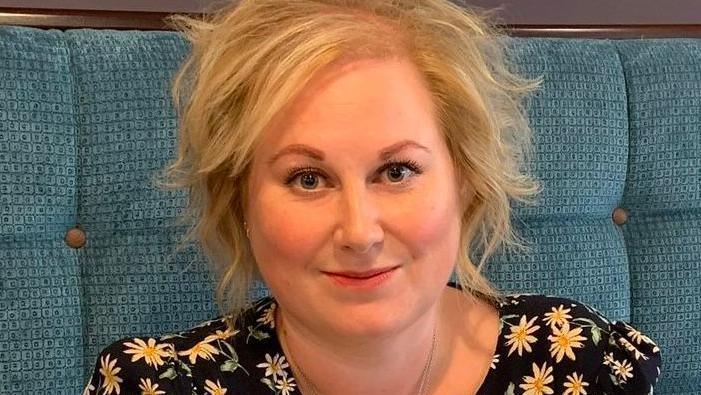 Gynaecology patient Amy smiles in a restaurant with a flowery top.