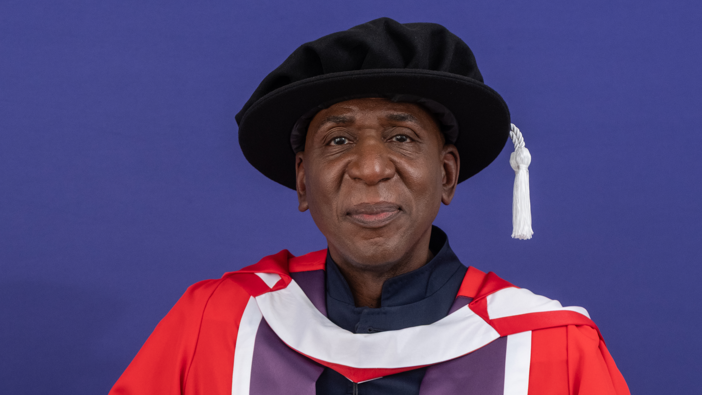 Head and shoulders of Colin McFarlane in a red and purple gown with a black hat on.