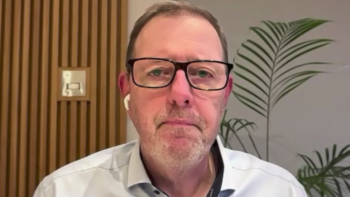 Mark McCall has short, thinning light brown hair sand is wearing black-framed glasses and a light shirt