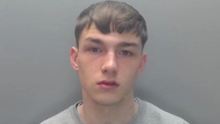 A mugshot of Jack Lawson, who is looking blankly into the camera. He has short brown hair and is wearing a grey jumper.