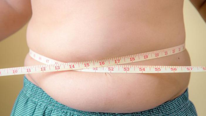 An overweight young boy holds a tape measure around his waist