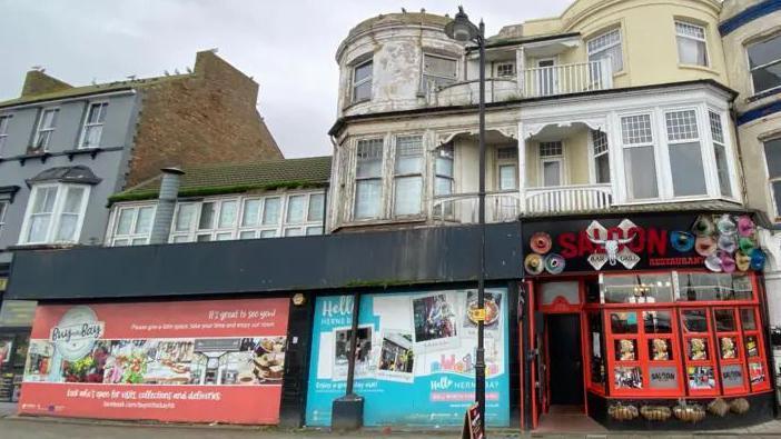 A decaying Regency-era building with boarded-up shops on the ground floor
