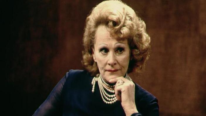 Fanny Cradock with her hand to her chin. She is wearing a pearl necklace