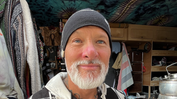 A close-up of Mark Myers. He is wearing a hat and has a grey beard. He is standing in front of his van.