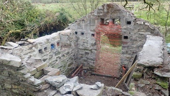 The building before it was repaired shows just four walls, no door and no roof.