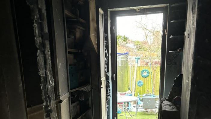 A view of the yard from the house through an open door. Some trampolines, a chair and a table can be seen.