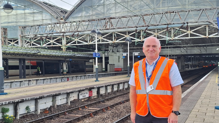 A man in a orange high-vis jacket standing on a platform at Leeds Station