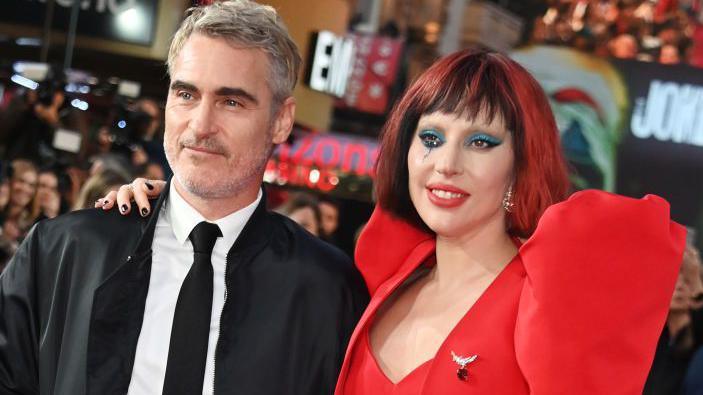 Actor Joaquin Phoenix wearing a black suit and tie and white shirt on a red carpet with Lada GaGa 