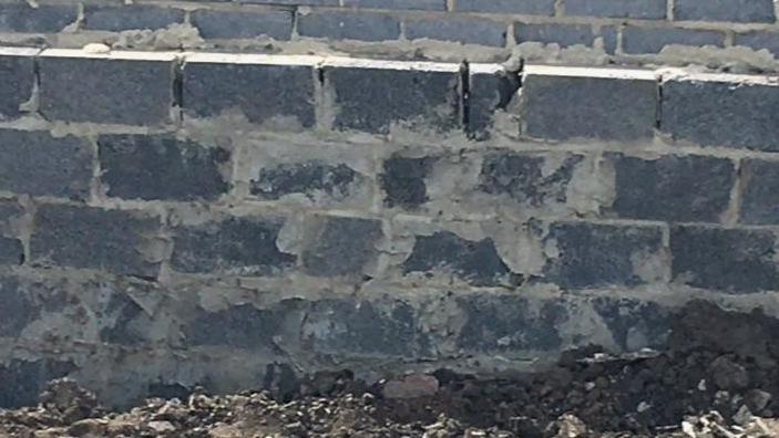 Foundations for a bungalow, showing grey breeze blocks with patchy cement or mortar. There are holes where cement or mortar should be, but isn't, and the mixtures is also spread across bricks in a messy way.