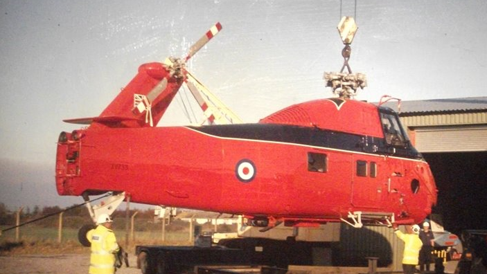 A red helicopter being lowered by a crane in the open air