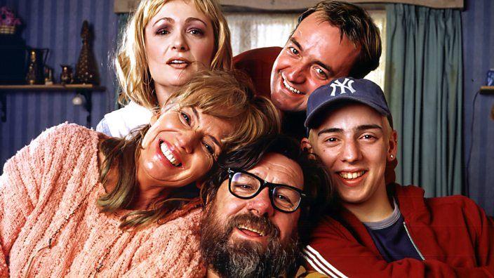 The Royle family posing together in their living room. Barbara is bottom left and leaning in on top of Jim.  Anthony is on the right with a baseball cap on, covering bleached hair.  Dave is leaning in behind him and Denise is behind Barbara on the left.